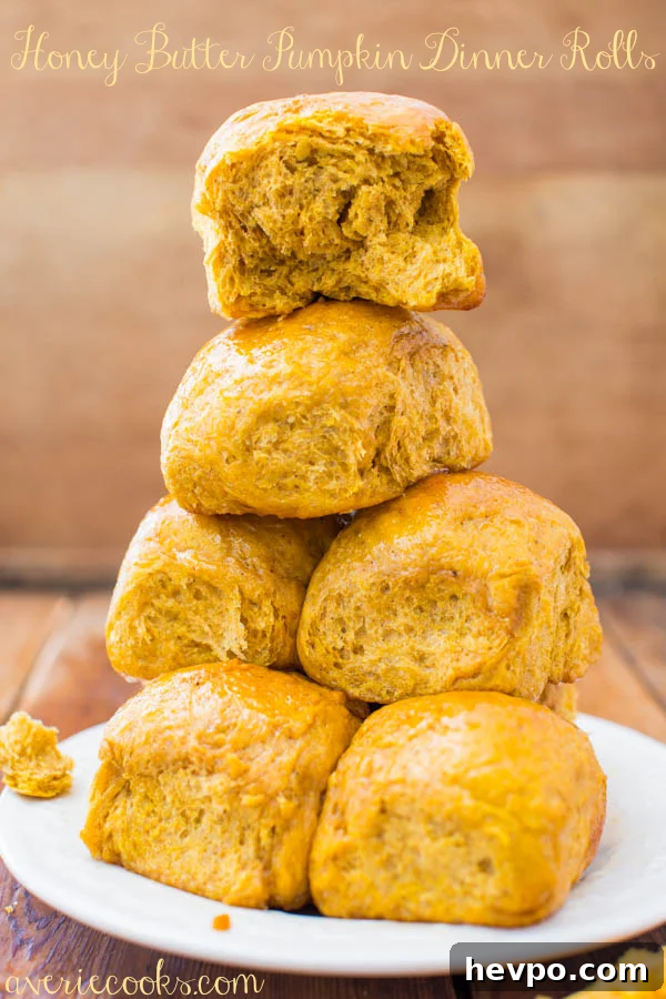 A stack of pumpkin dinner rolls on a plate. 