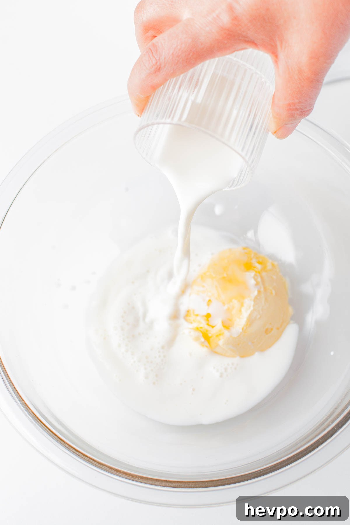 Milk being poured into a bowl with ingredients for bread rolls. 
