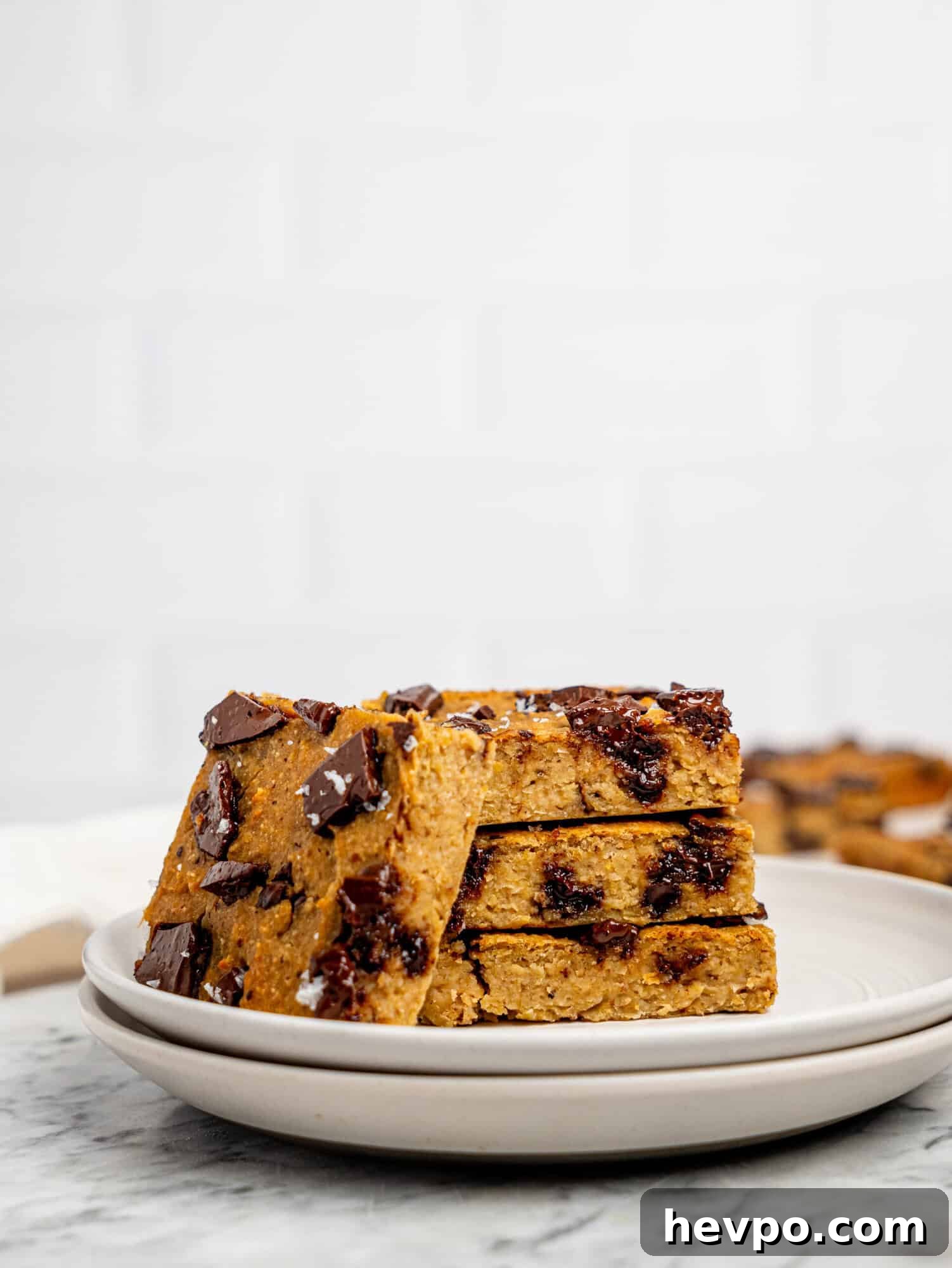 Chewy Chickpea Cookie Bars with Gooey Chocolate Swirls 2 Healthy cookie bars with dark chocolate stacked on a white plate.