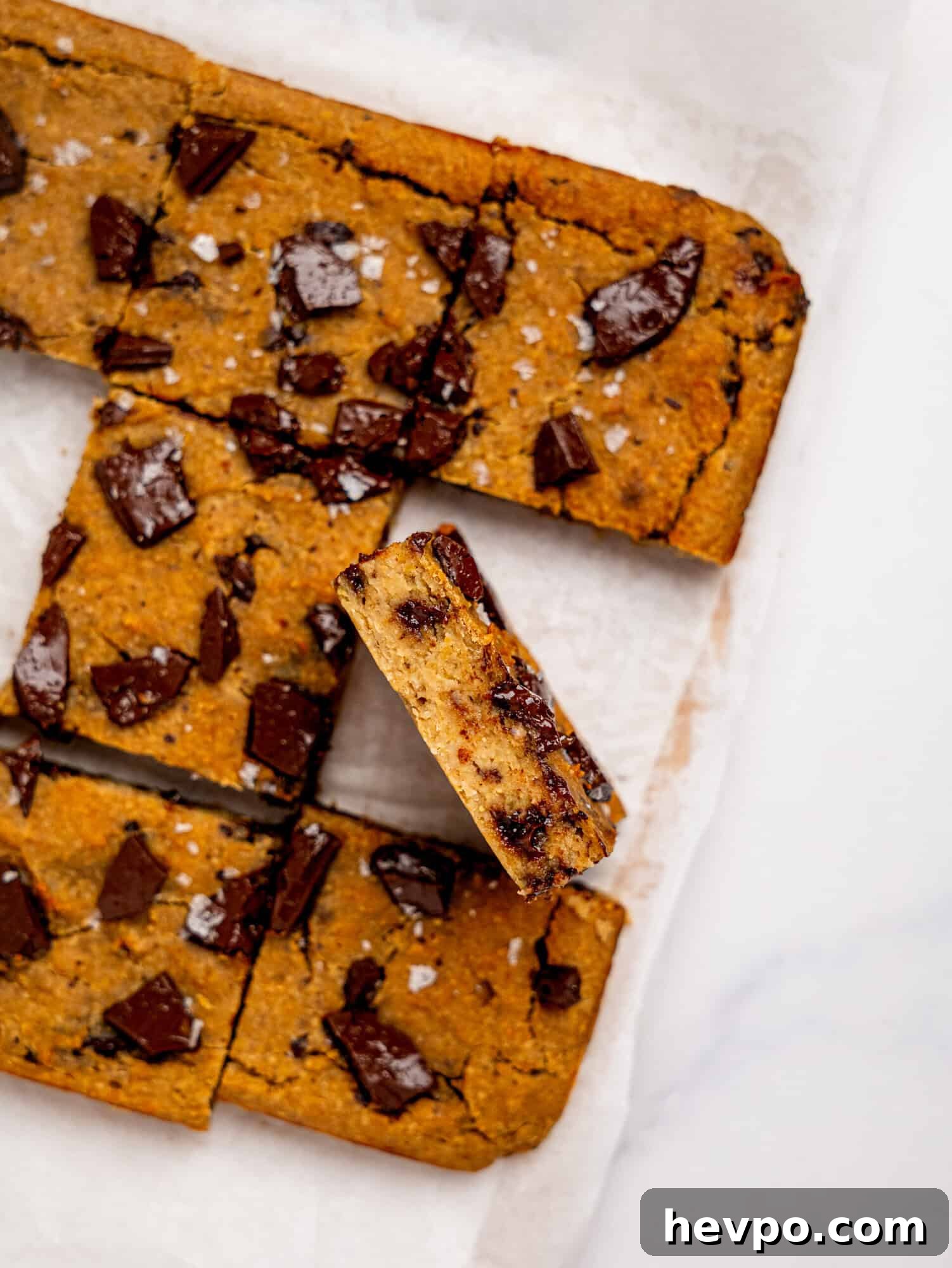 Chewy Chickpea Cookie Bars with Gooey Chocolate Swirls 6 Bird's eye view of chickpea cookie bars on a sheet of white parchment paper, one is turned on its side to reveal the fudgy texture.