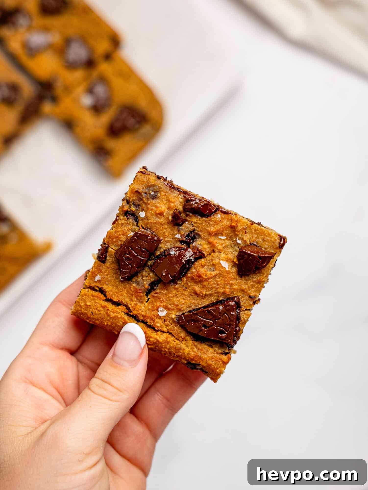 Chewy Chickpea Cookie Bars with Gooey Chocolate Swirls 7 A hand holding a chickpea cookie bar with dark chocolate.