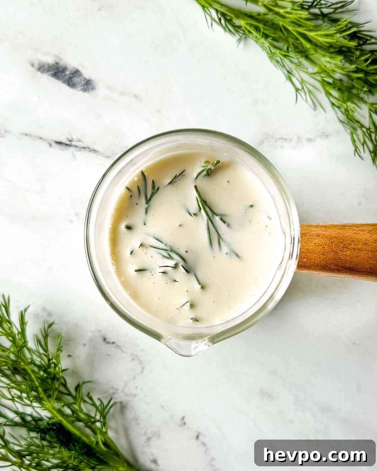 Creamy Dill Sauce for Fish, Salmon, and Vegetables 2 closeup of dill sauce in a glass container with a wooden handle on a white marble counter.