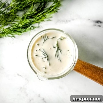 Creamy Dill Sauce for Fish, Salmon, and Vegetables 7 closeup of dill sauce in a glass container with a wooden handle on a white marble counter.