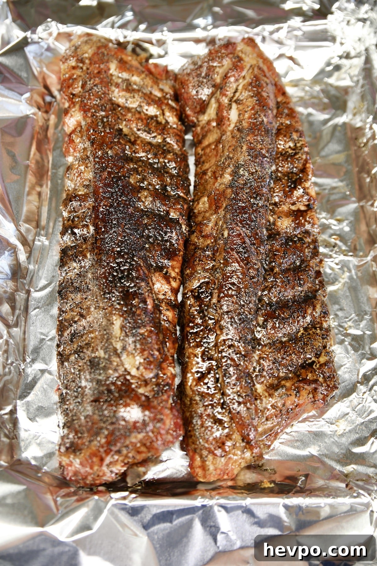 2 racks baby back ribs with orange bbq sauce on foil line pan.