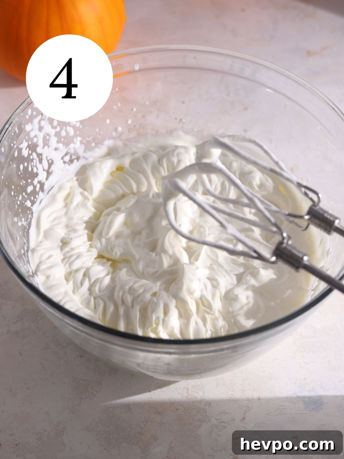 Creamy Pumpkin Ice Cream Recipe for Fall Desserts 7 Whipped cream in a glass bowl with electric beaters next to it.