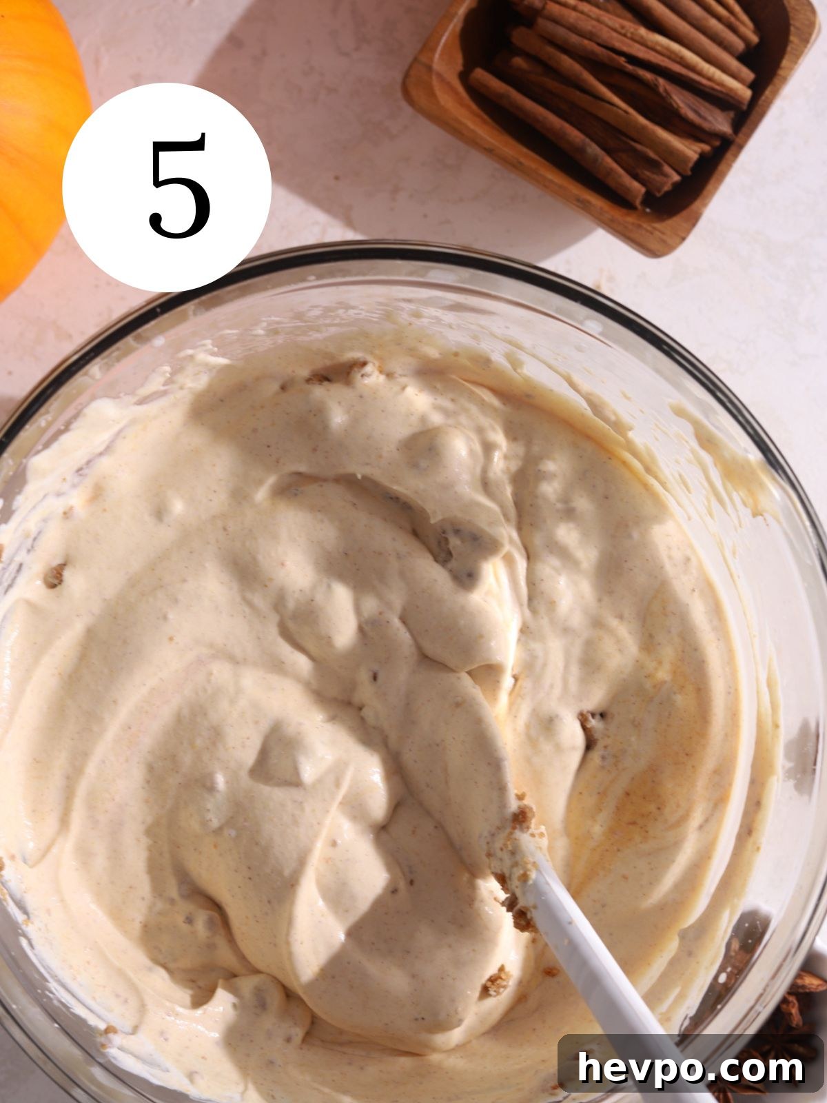 Creamy Pumpkin Ice Cream Recipe for Fall Desserts 8 A glass bowl with pumpkin ice cream mixture stirred together with a whisk.