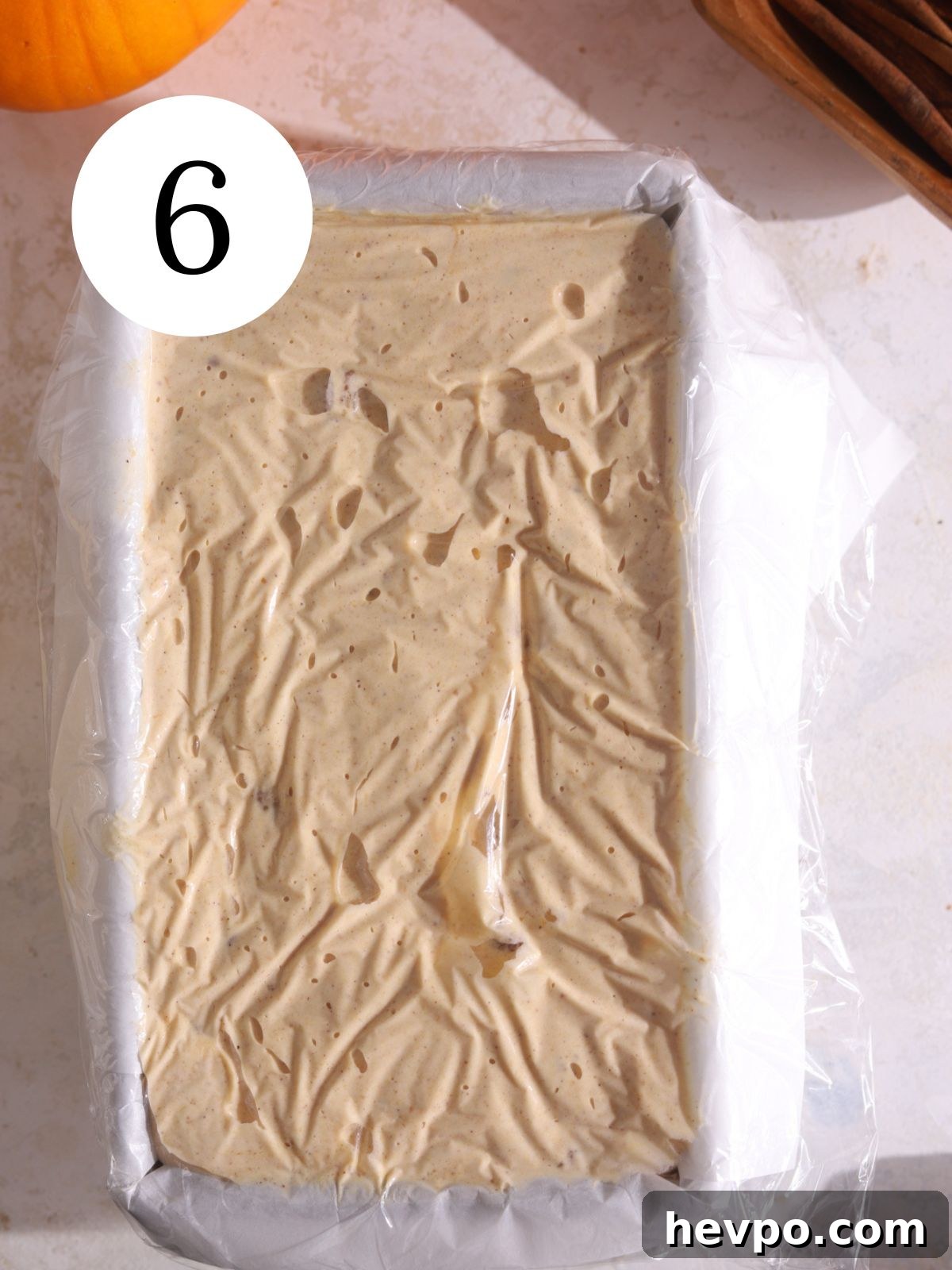 Creamy Pumpkin Ice Cream Recipe for Fall Desserts 9 Pumpkin ice cream mixed together in a loaf pan covered with plastic wrap.