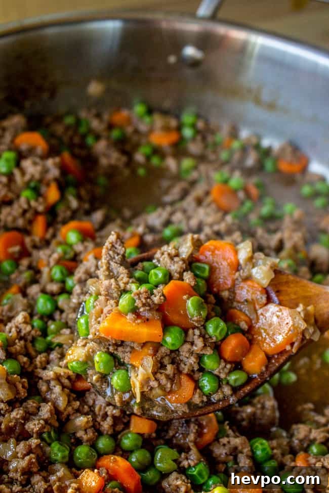 Cooking the filling cooking peas, carrots, and onions with ground beef.