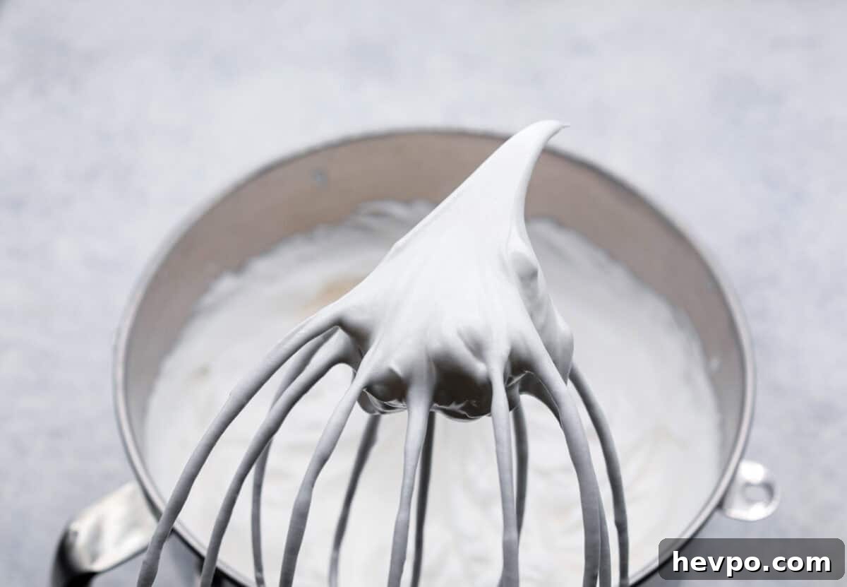 Whip until medium-stiff peaks. Angle shot of whisk with peaked egg whites on top.