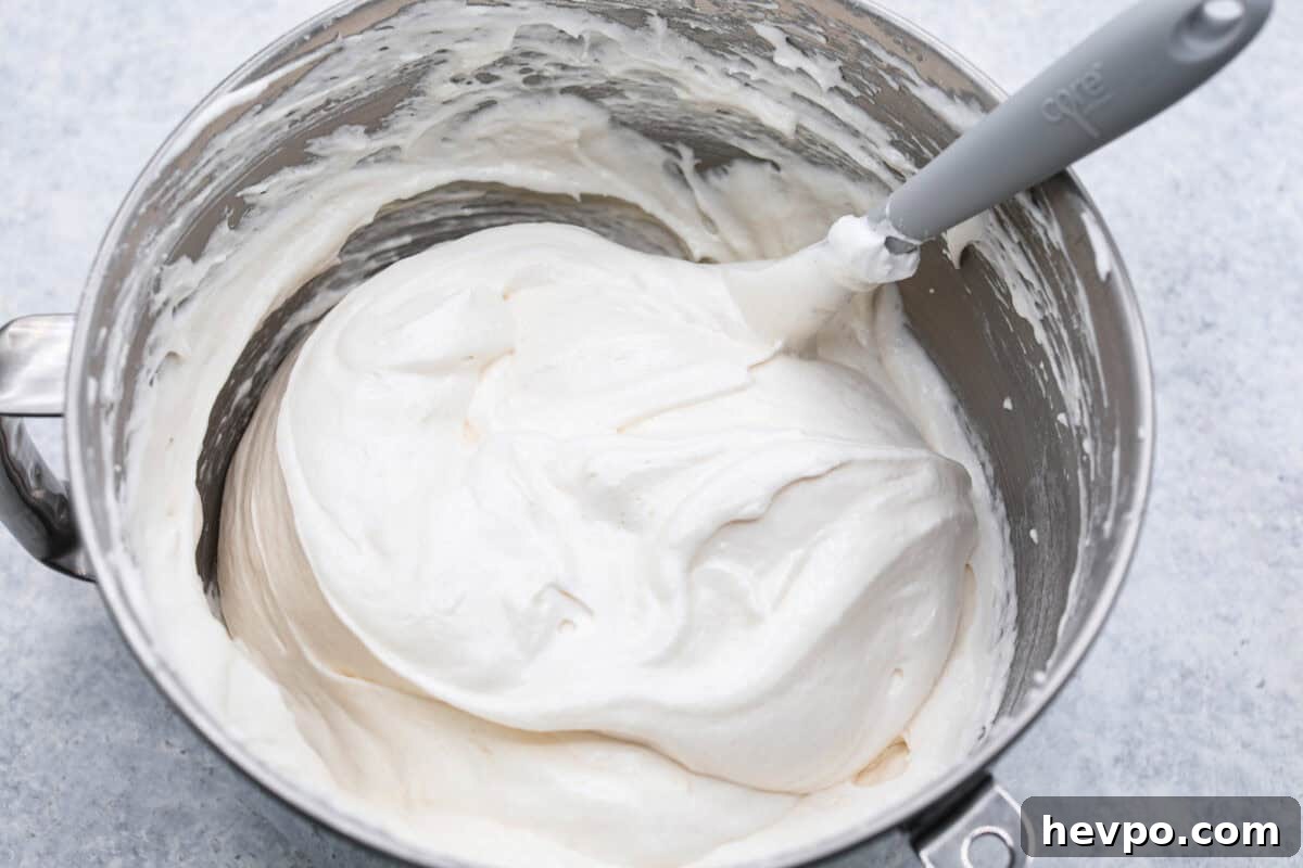 Fold in the flour and salt. Overhead shot of bowl of egg whites with a spatula folding in flour.