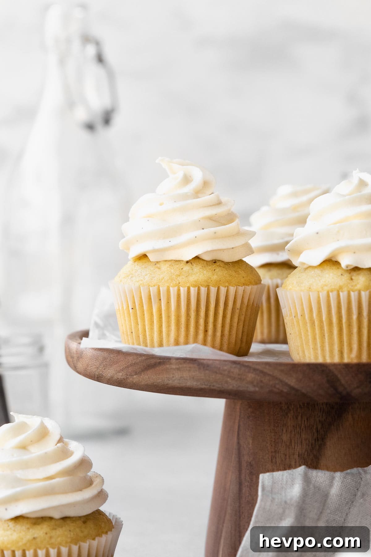 Side on shot of vanilla buttercream topped vegan cupcakes on a wooden cake platter.