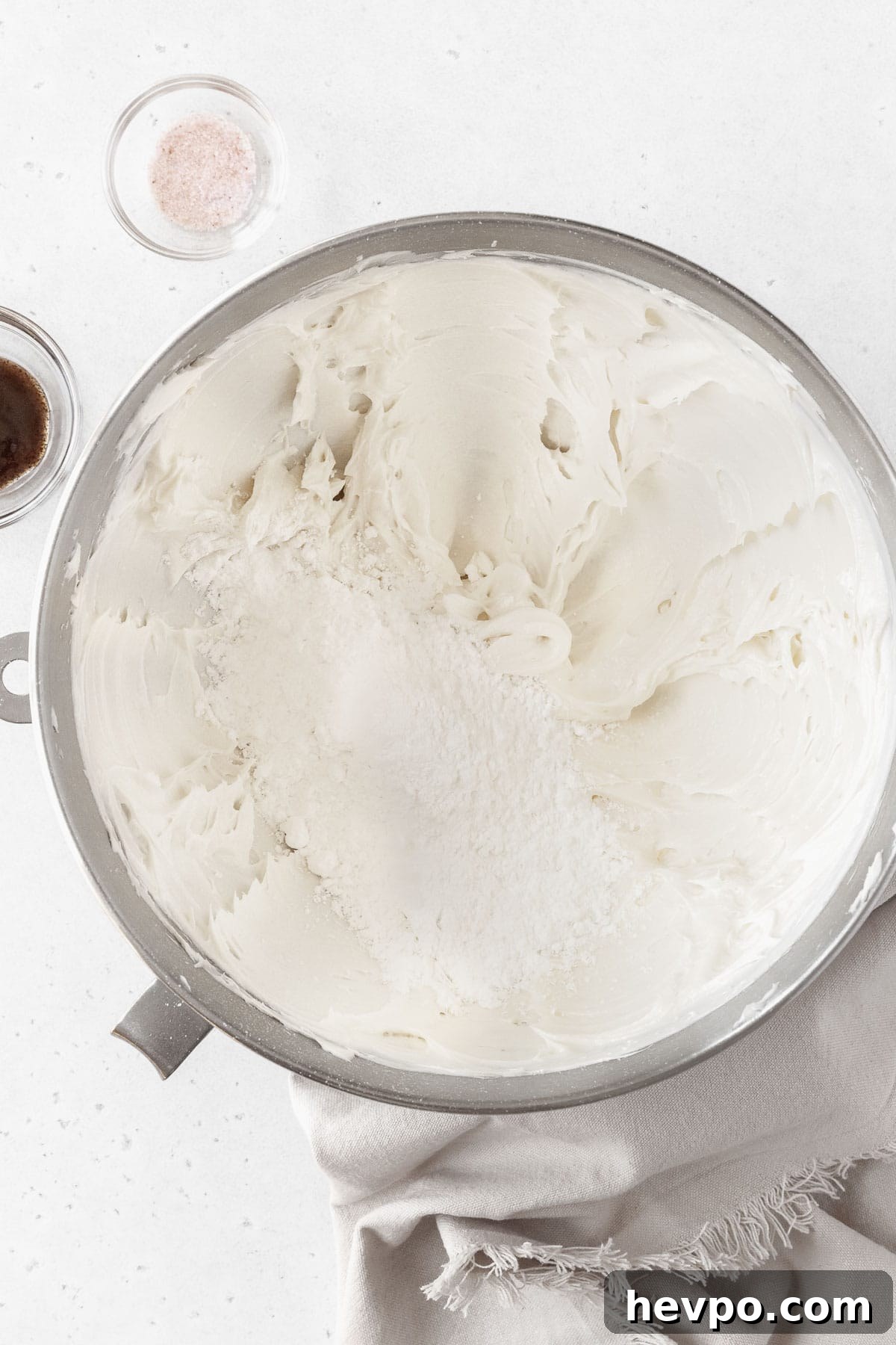 Powdered sugar being added to the large bowl of whipped butter.