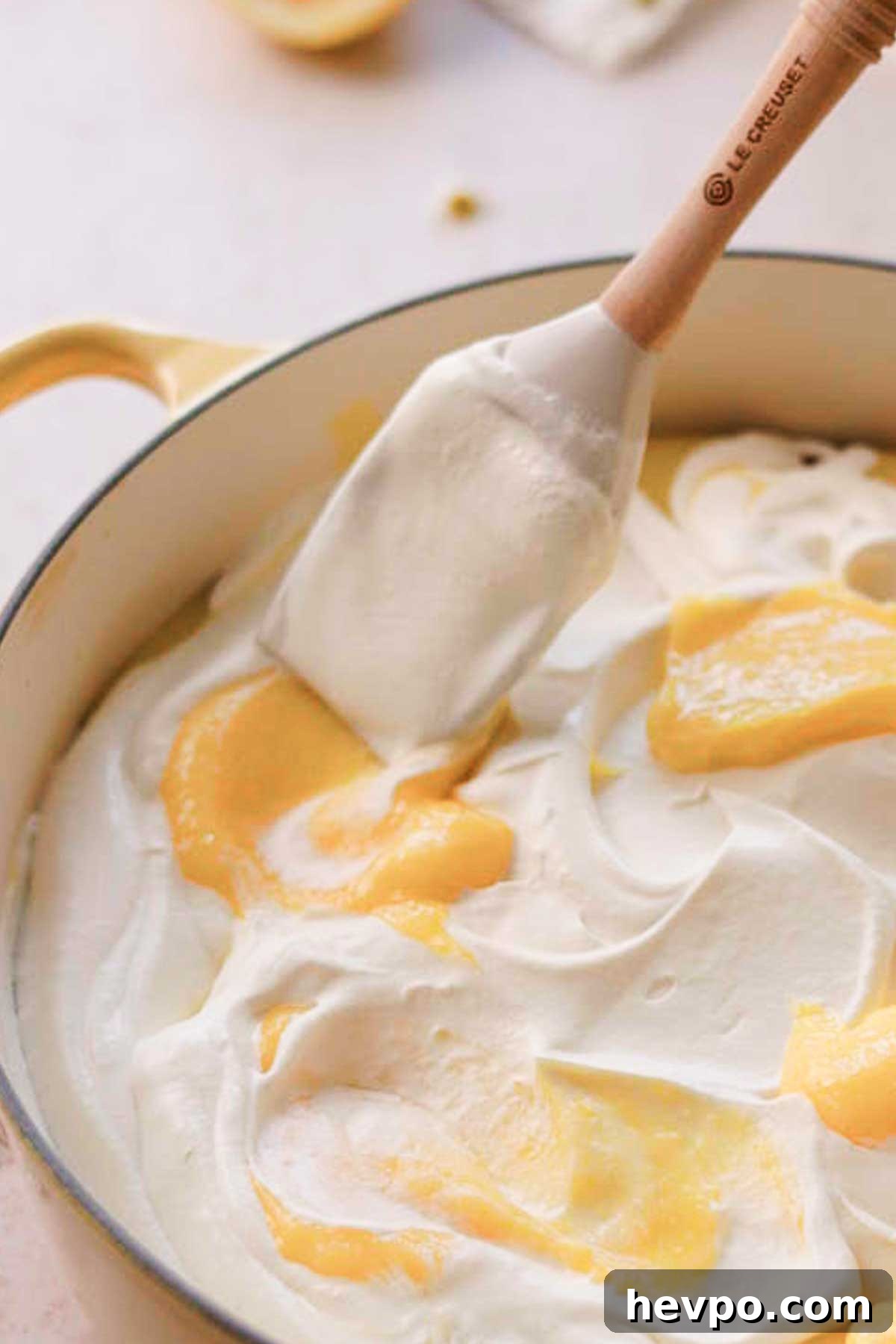 Moist Lemon Poke Cake Recipe with Zesty Lemon Glaze 18 swirling lemon curd on top of whipped cream with a spatula