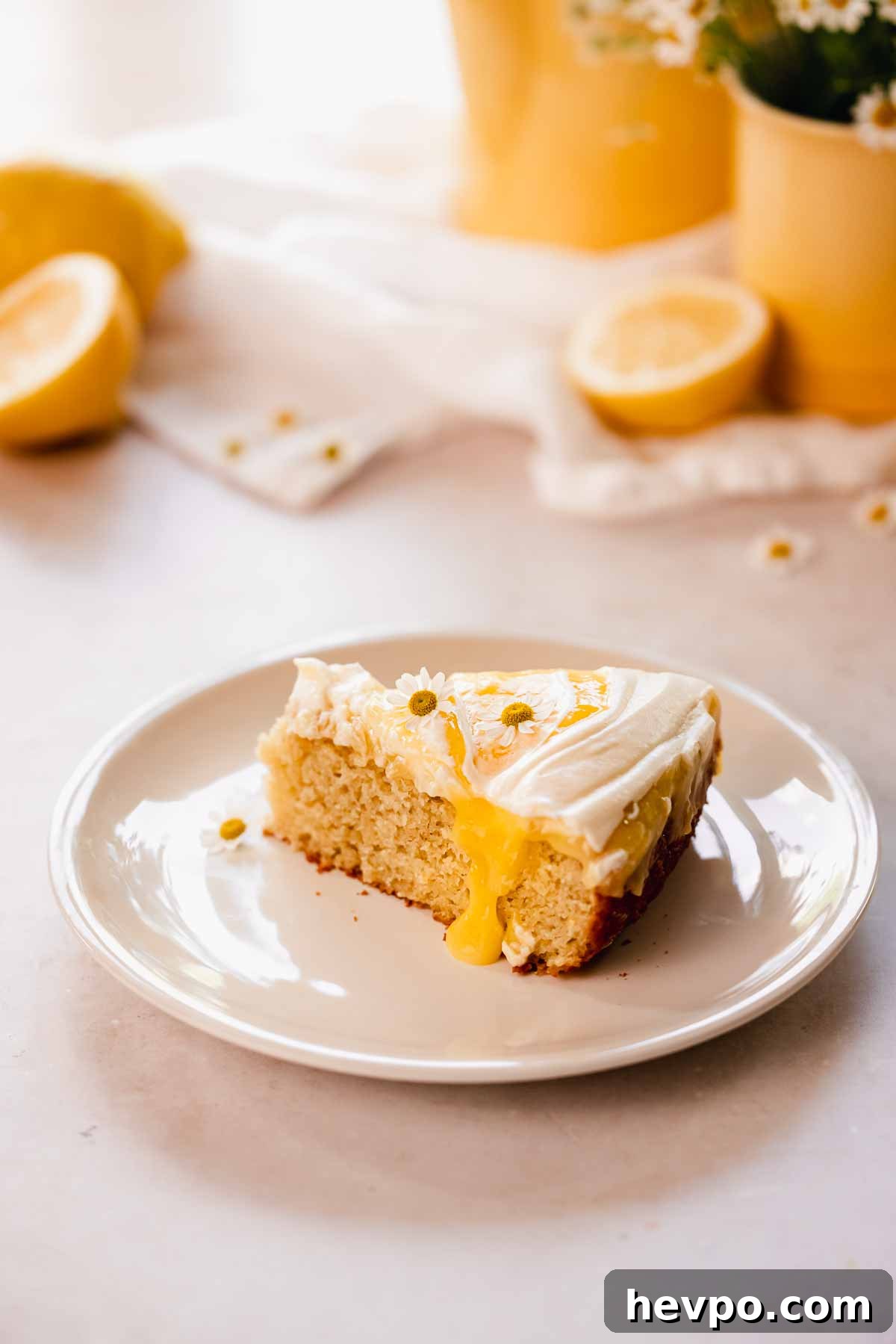 Moist Lemon Poke Cake Recipe with Zesty Lemon Glaze 3 a slice of decorated lemon poke cake with lemon curd oozing from under the whipped cream