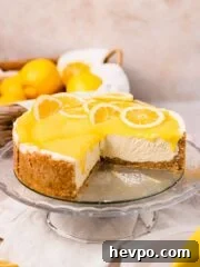 lemon curd cheesecake on glass cake stand topped with lemon curd with a wedge cut out