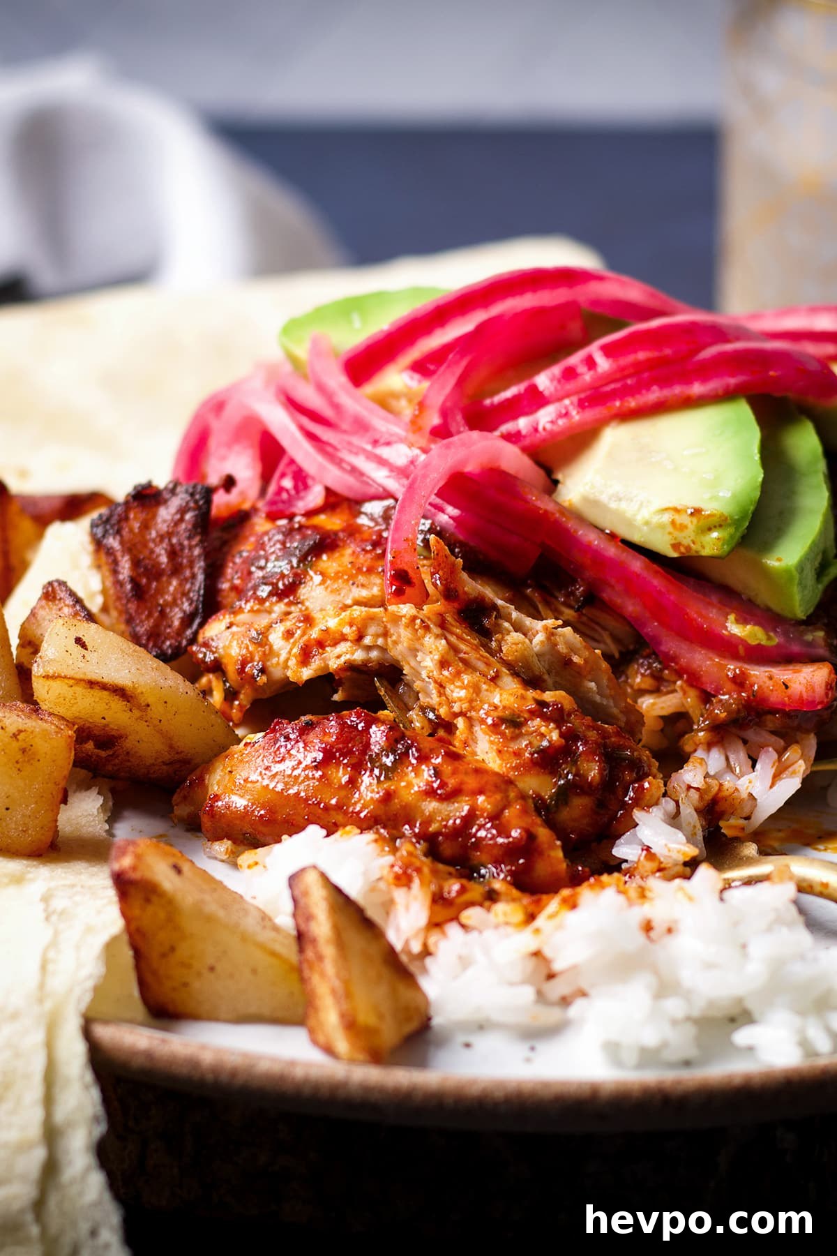 A white plate filled with white rice topped with Mexican Adobo Chicken, fried potatoes, and a flour tortilla.