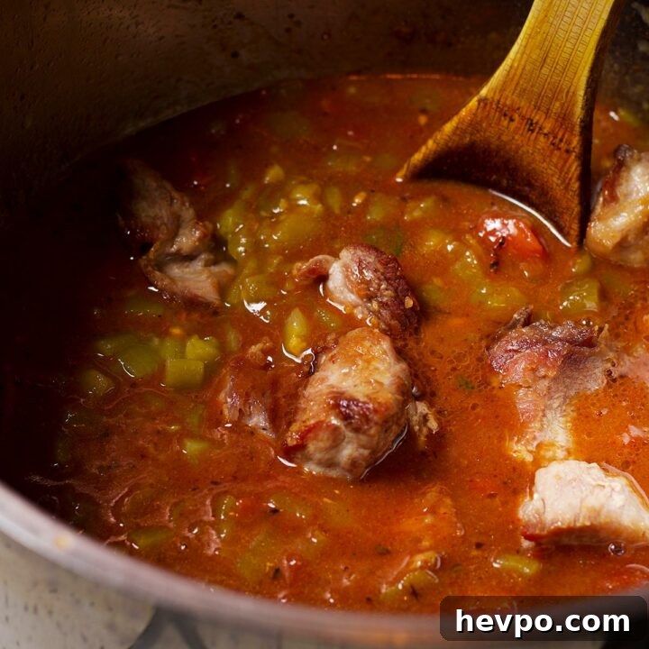 Using a wooden spoon to stir a pot of green chili as it simmers on the stovetop.