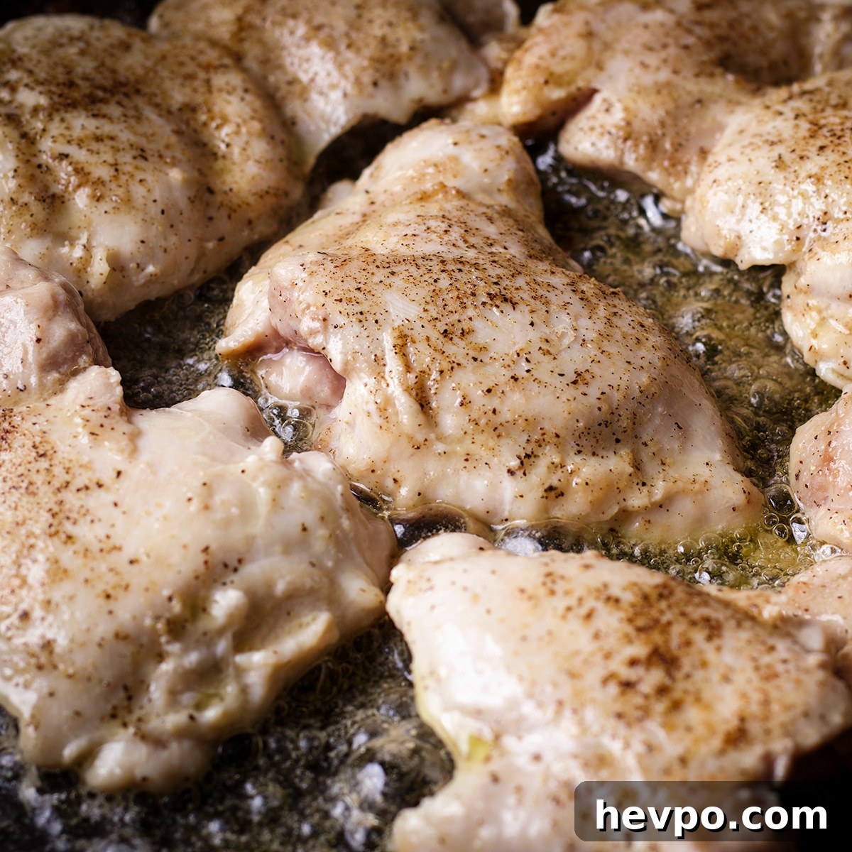 Boneless, skinless chicken thighs cooking in hot butter and oil until they are browned on the outside.