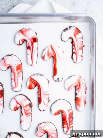White and red icing swirled candy cane shaped sugar cookies on a parchment paper lined silver baking sheet.