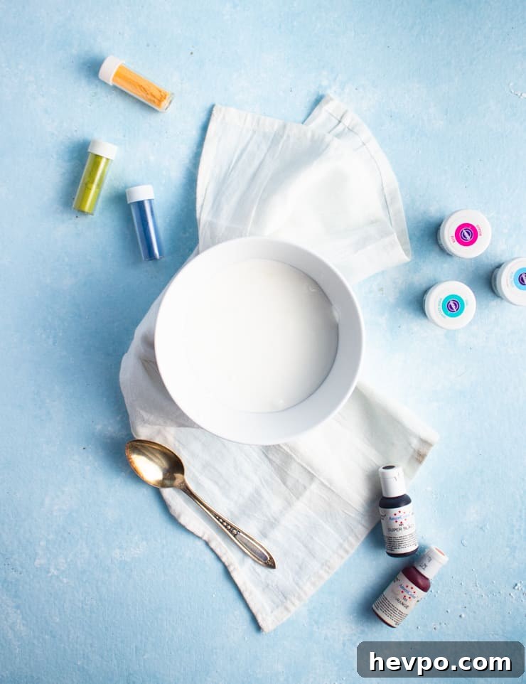 a bowl of white royal icing with food coloring bottles around it