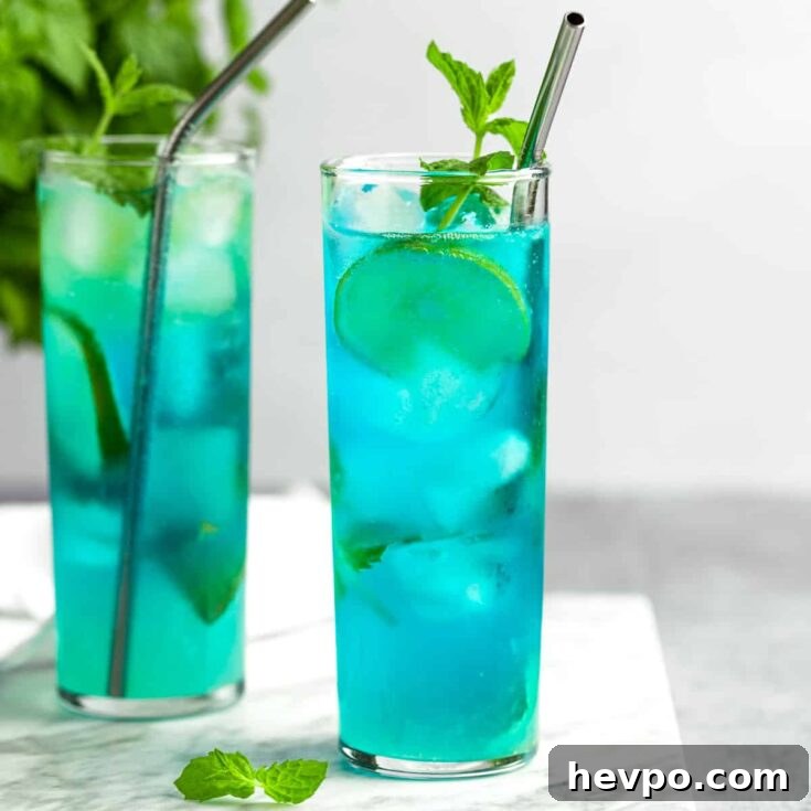 A couple blue mojitos garnished with lime slices and mint leaves.