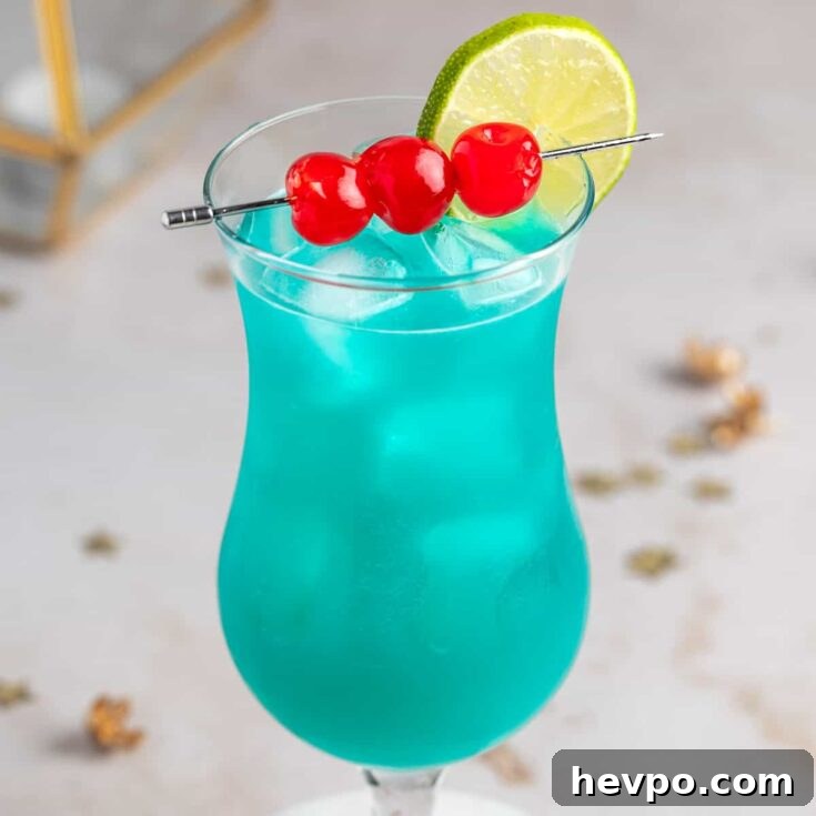 A blue hurricane drink garnished with maraschino cherries and a lime slice, on a marble table.