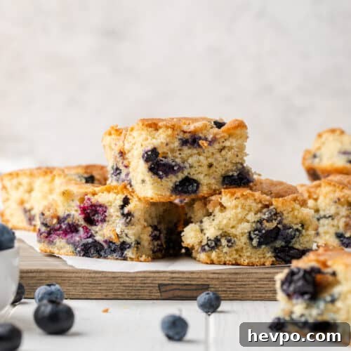 Three slices of gluten free blueberry cake stacked on a wooden cutting board.