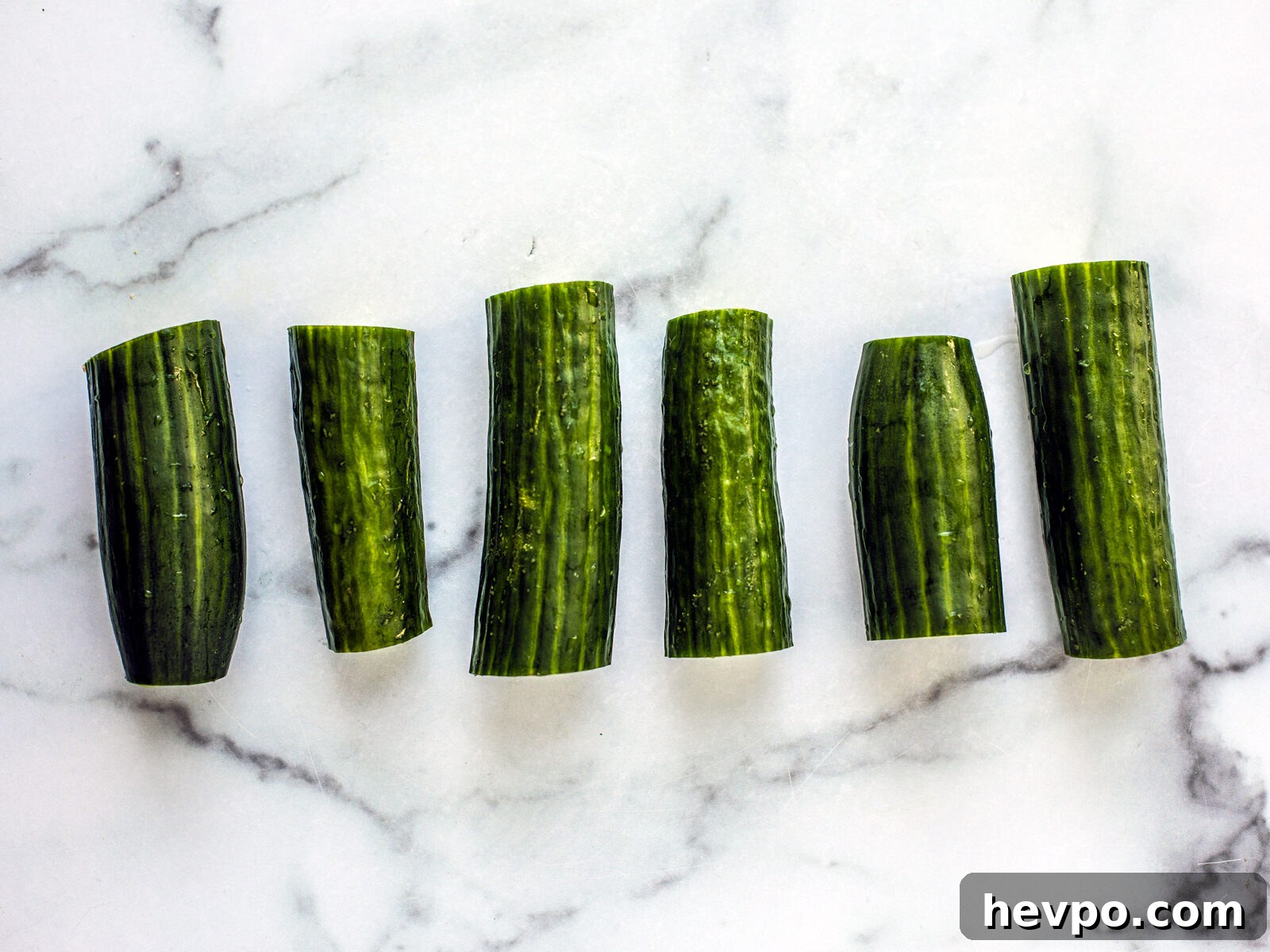 Six cucumber cuttings on marble counter set up in a line.