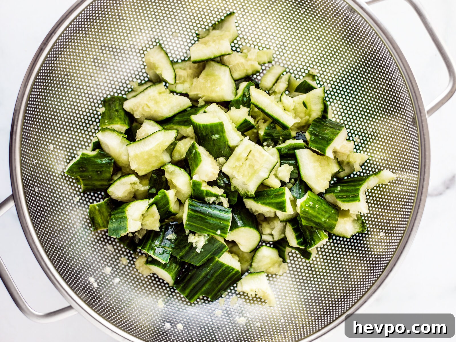 Smashed cucumber bits in a colander.