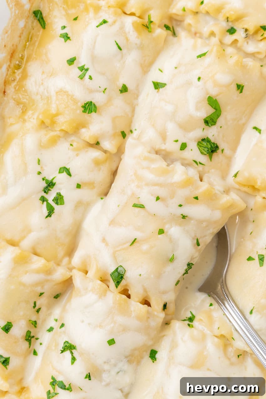 Creamy White Chicken Lasagna Roll-Ups Recipe 11 a silver spoon scooping a white chicken lasagna roll up out of a white baking dish