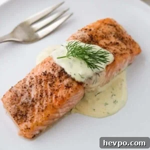 Close up of baked salmon topped with Warm Mustard Dill Sauce and a sprig of dill.