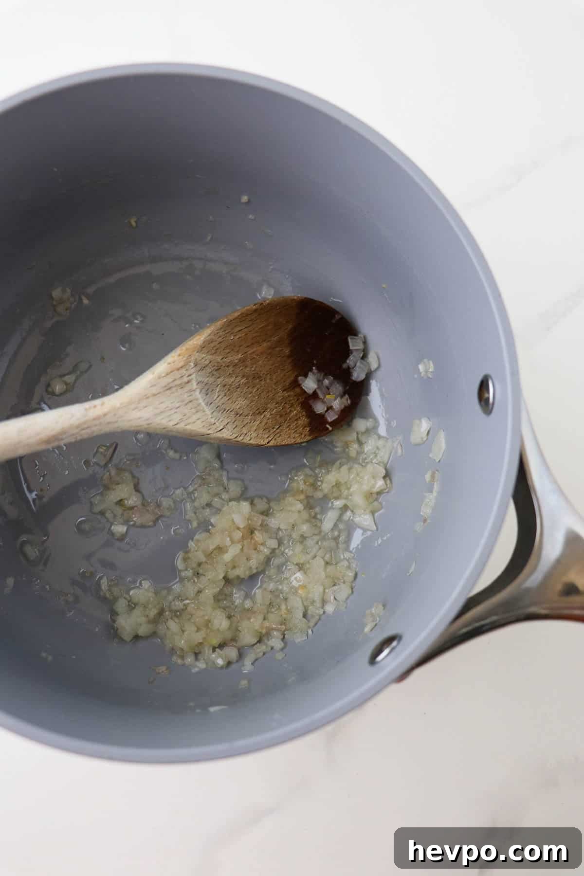 Cooked minced shallots in a saucepan with a wooden spoon.