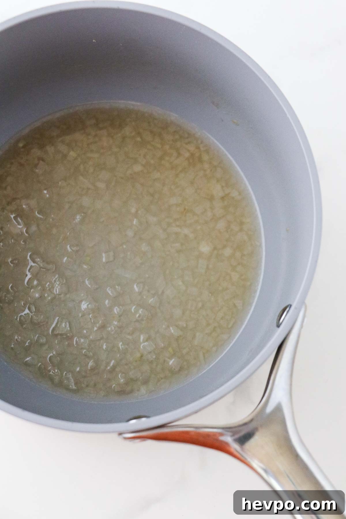 Minced shallots and wine cooking in a gray saucepan.