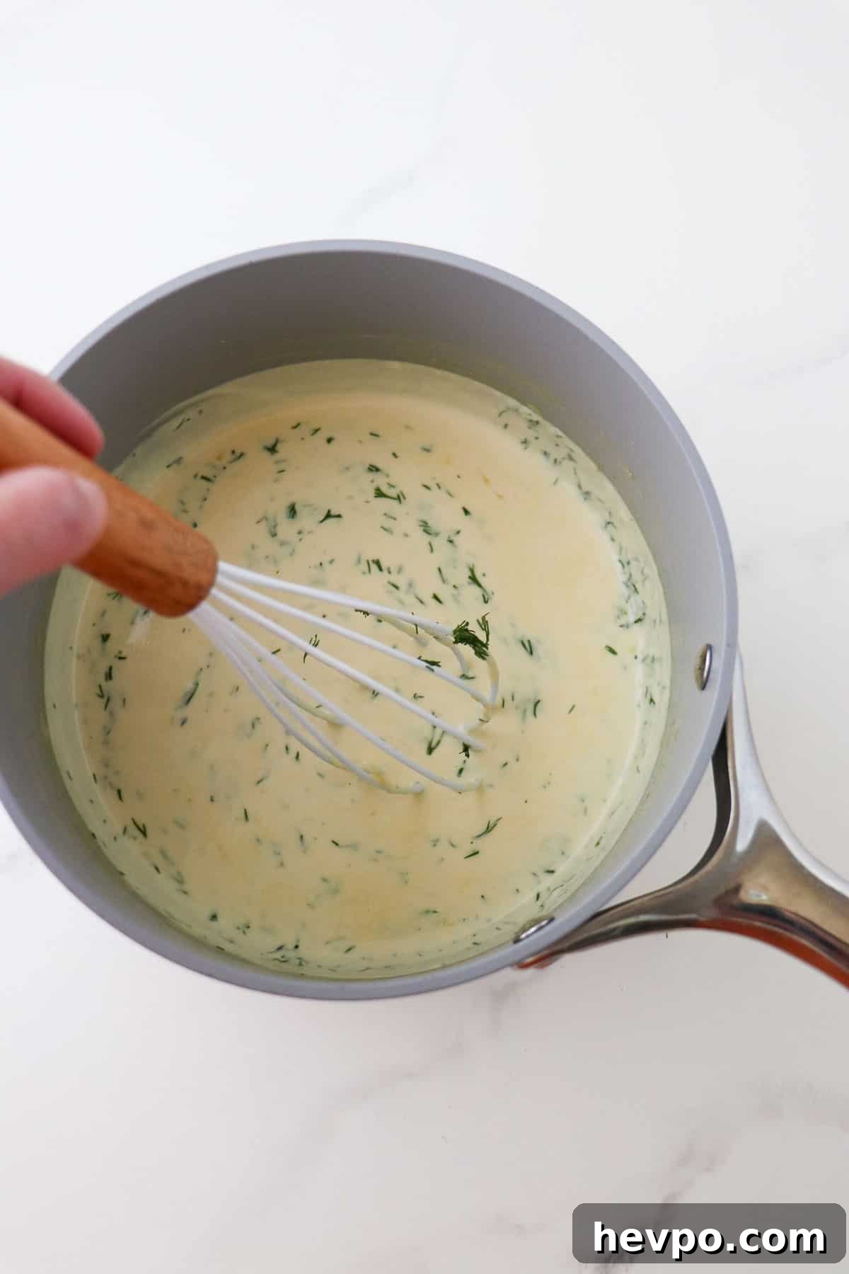 Warm Mustard Dill Sauce in a gray saucepan with a whisk.