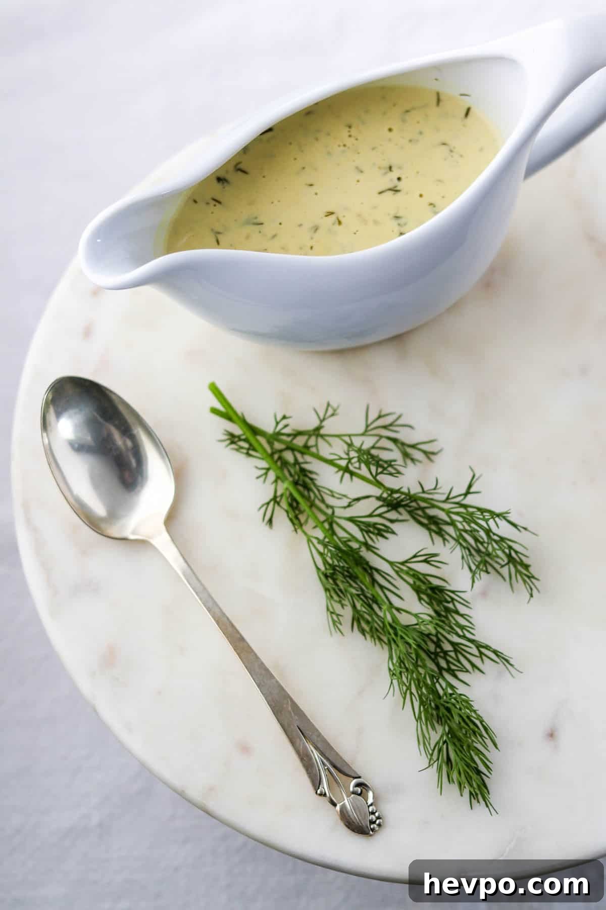 Warm Mustard Dill Sauce in a gravy boat next to a spoon and a sprig of dill.