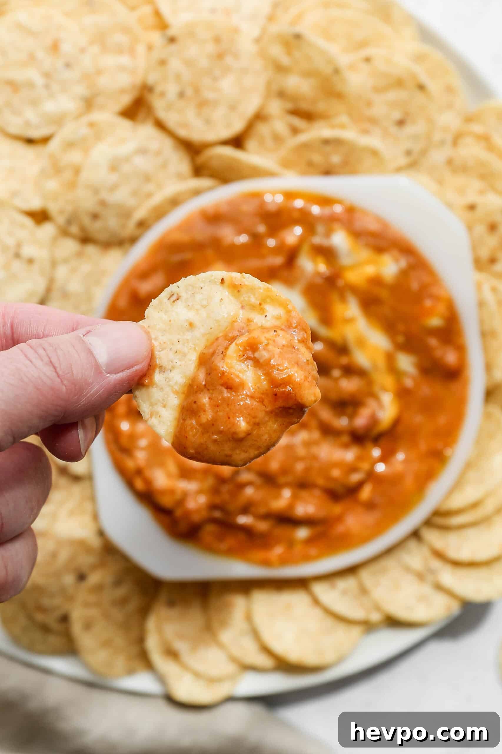 Cheesy Pinto Beans (Gluten-Free) — Creamy Mexican-Style Recipe 3 a white bowl of gluten free cheesy pinto beans surrounded by round tortilla chips with me holding a chip with dip on it.
