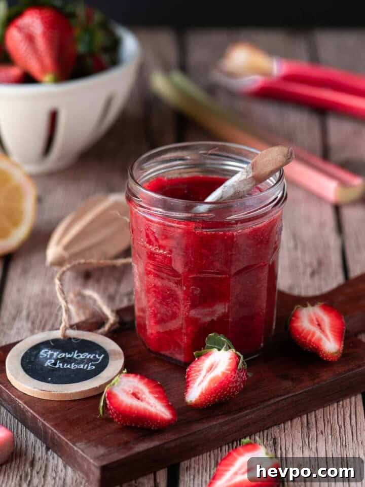 Small-Batch Strawberry Rhubarb Jam Recipe for Perfect Preserves 2 Strawberry rhubarb jam in a clear jar on a wood surface with fruit around it.