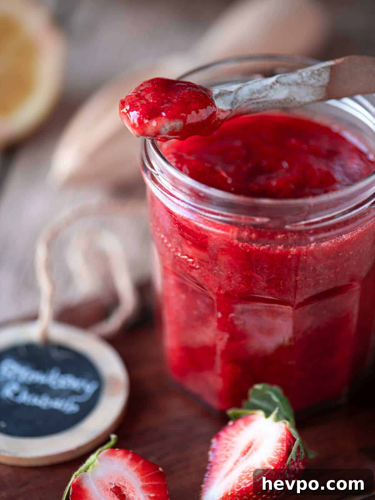 Small-Batch Strawberry Rhubarb Jam Recipe for Perfect Preserves 5 Close up of a spoon dipped into strawberry jam in a clear jar.