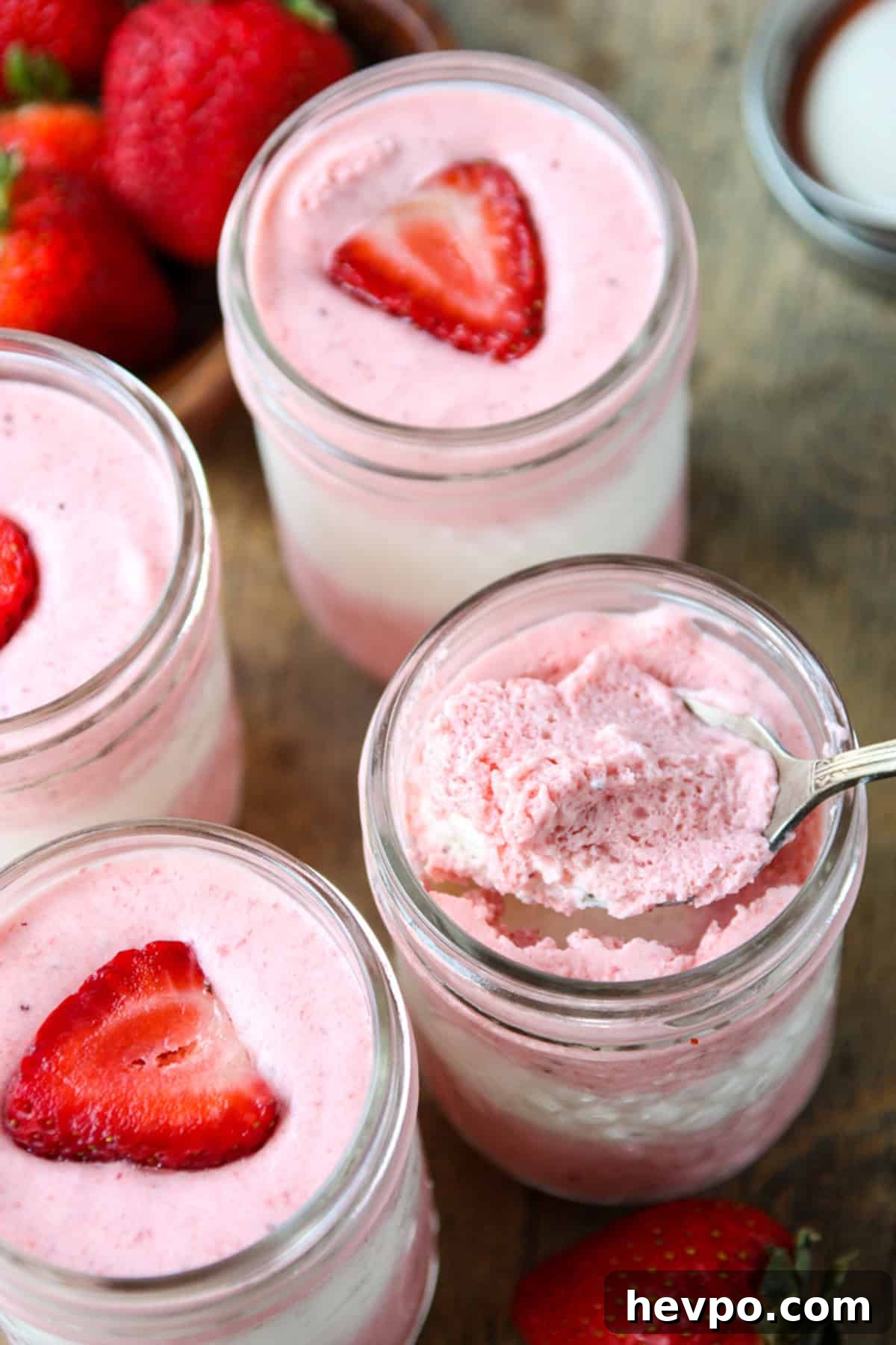 A spoonful of layered strawberry mousse being scooped from a jar.