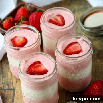 jars of mousse with pink and white layers topped with fresh strawberry slices in mason jars