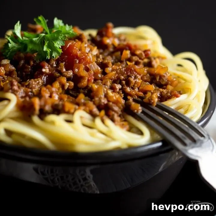 Easy spaghetti bolognese in a black bowl with a fork, topped with parsley