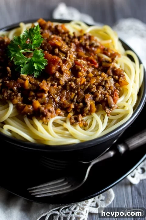 Easy spaghetti bolognese in a black bowl with a fork, topped with parsley
