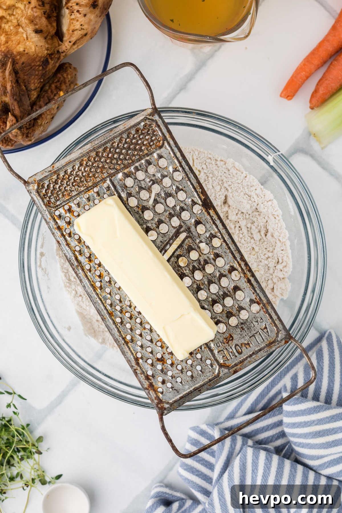 A grater with a stick of butter, being grated into a bowl of flour.