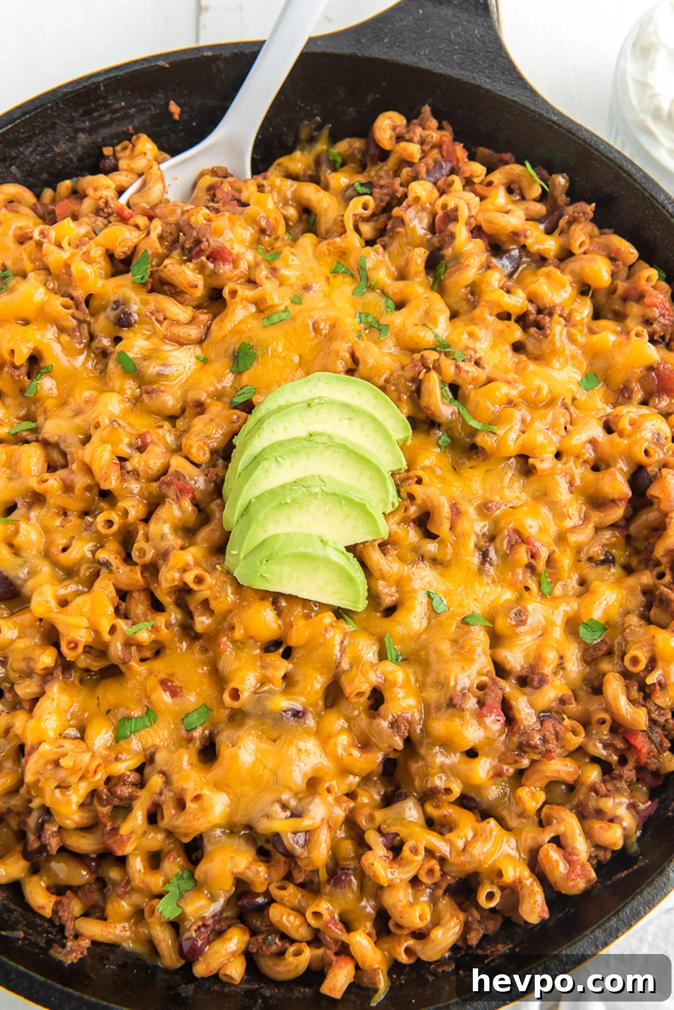 Hearty Chili Mac Recipe: Quick Comfort Food for Weeknights 8 Chili mac in a skillet with a spoon scooping in and sliced avocados on top.
