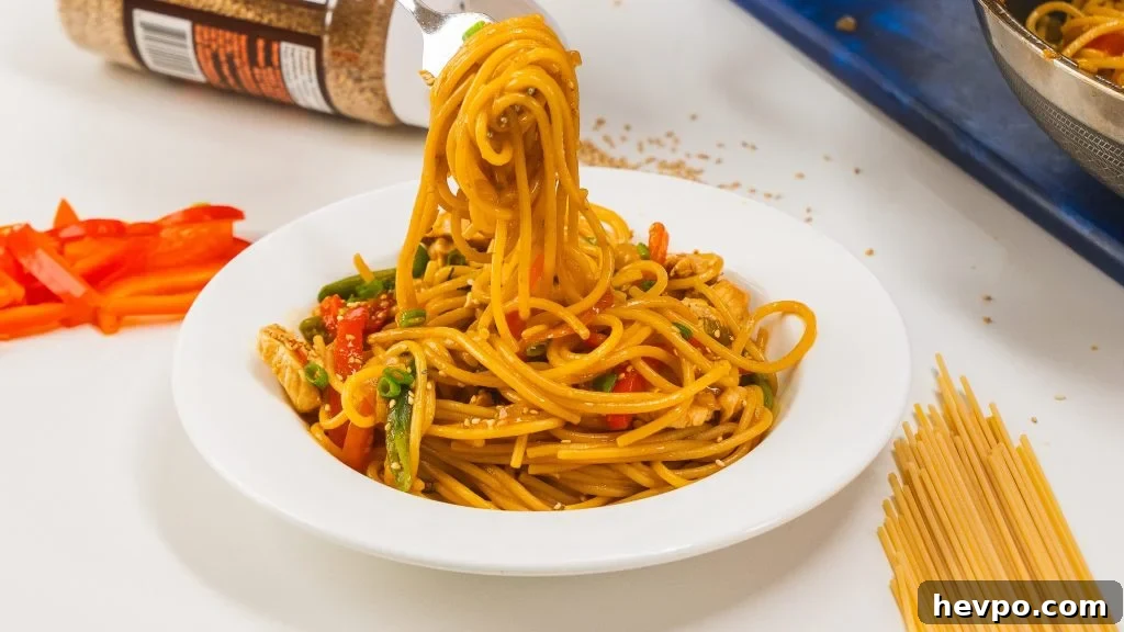 Homestyle Chicken Noodle Stir-Fry That Beats Takeout 3 Noodles in a white bowl with a fork over top twirling some of the noodles.
