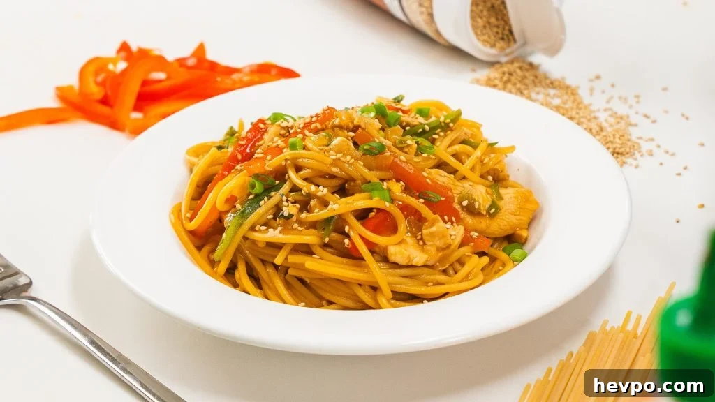 Homestyle Chicken Noodle Stir-Fry That Beats Takeout 4 Stir fry in a white bowl. Snap peas, red pepper and dry pasta is visible to the side.