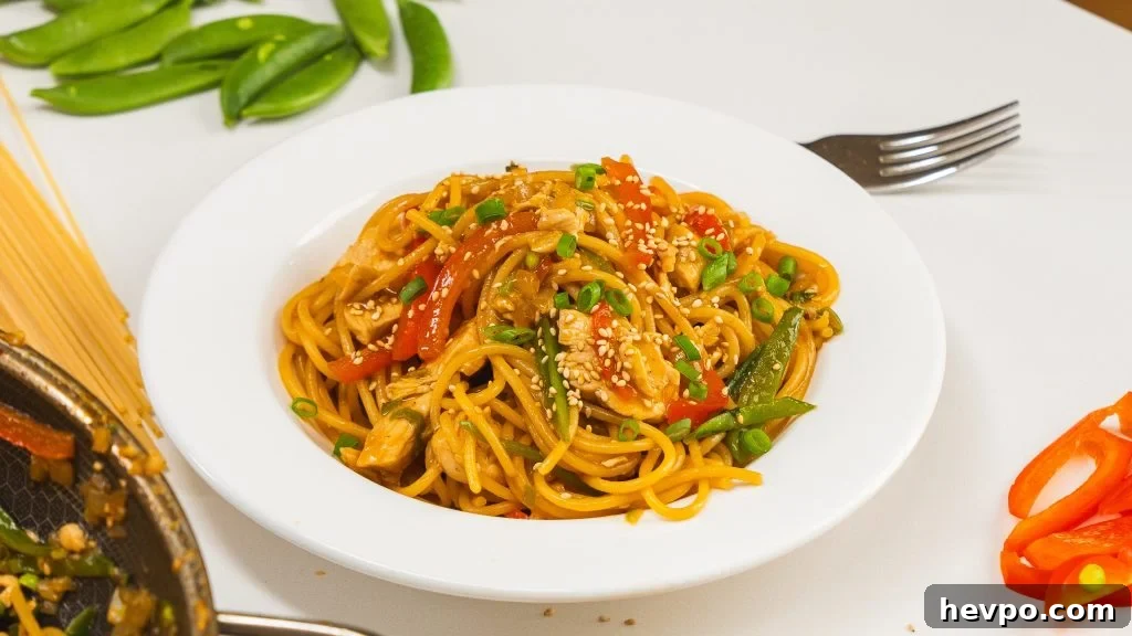 Homestyle Chicken Noodle Stir-Fry That Beats Takeout 7 One pan chicken noodle stir fry recipe in a white bowl with green onion and sesame seeds on top.