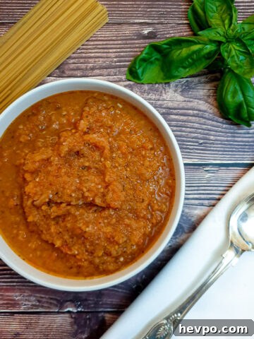 A dish of marinara sauce on a table next to a pile of uncooked spaghetti.