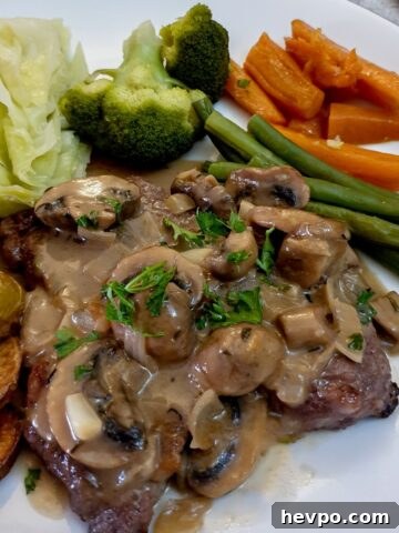 Marsala mushroom sauce poured over a steak on a plate with vegetables.
