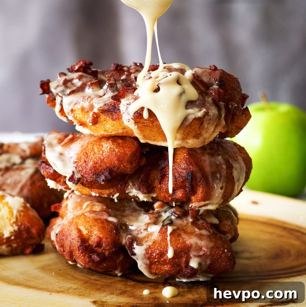 Maple glaze dripping down the side of a stack of three homemade apple fritters.